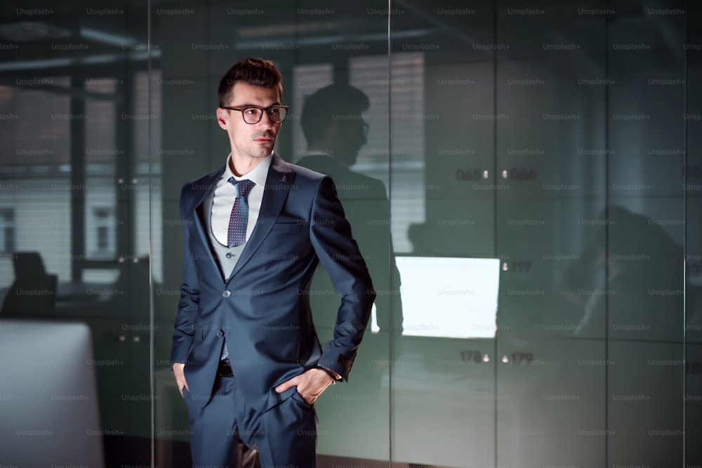 A portrait of young businessman standing in an office, hands in pockets. Copy space.