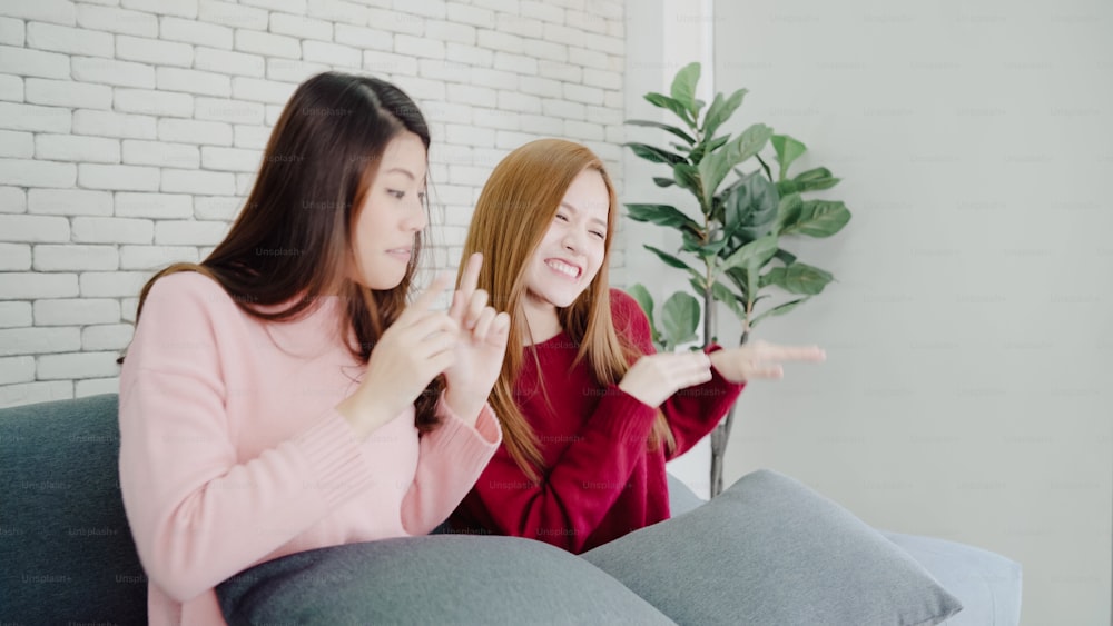 Lesbian Asian couple sing a song and dancing in living room at home, sweet couple enjoy funny moment while lying on the sofa when relax at home. Lifestyle couple relax at home concept.