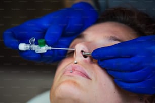 Portrait of a woman getting her nose pierced. Man showing a process of piercing nose with steril neadle and latex gloves