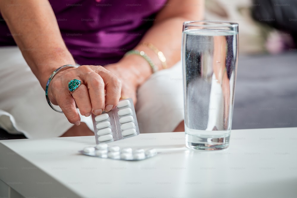 Close Up Of Senior woman Taking Calcium supplement tablet pills and Omega 3 oil with glass of water.Nutritional Supplements.Sport,Diet Concept.Capsules Vitamin And Dietary Supplements.