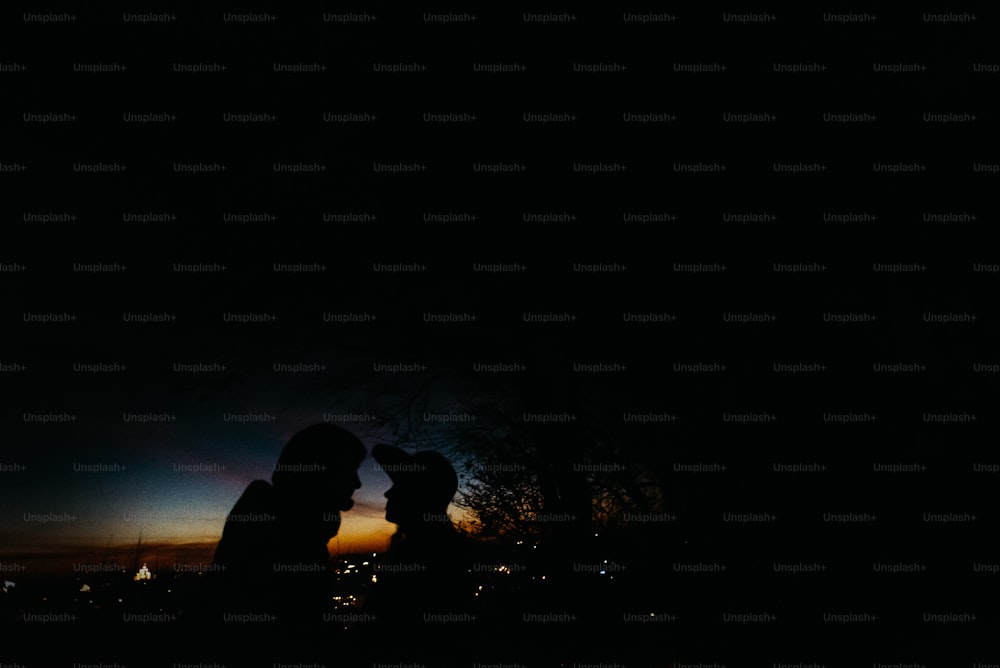 silhouette d’un couple heureux se regardant et se touchant avec douceur sur le fond du ciel de coucher de soleil et des lumières de la ville