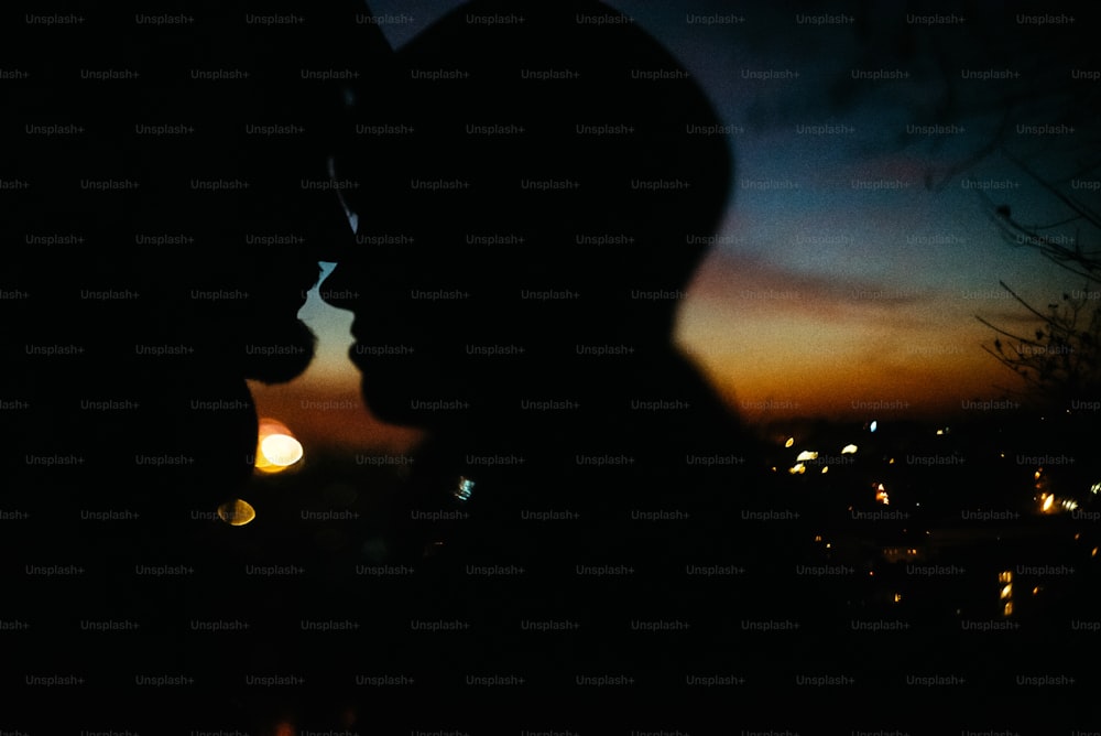 silhouette of happy couple looking at each other and touching with gentle on background of sunset sky and city lights