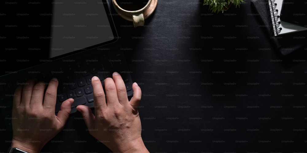 Top view of man's hands typing on laptop with black leather table in modern workspace