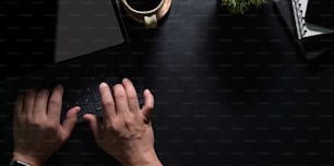 Top view of man's hands typing on laptop with black leather table in modern workspace