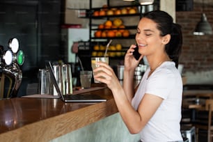 Young charming woman calling with cell telephone while sitting alone in coffee shop during free time, attractive female with cute smile having talking conversation with mobile phone while rest in bar