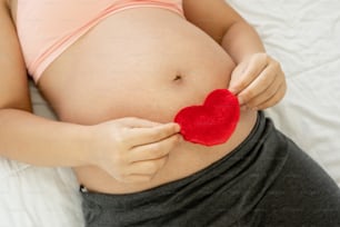 Schwangere Frau, die sich zu Hause glücklich fühlt, während sie sich um ihr Kind kümmert. Die junge werdende Mutter hält Baby im schwangeren Bauch. Schwangerschaftsvorsorge und Schwangerschaftskonzept für Frauen.
