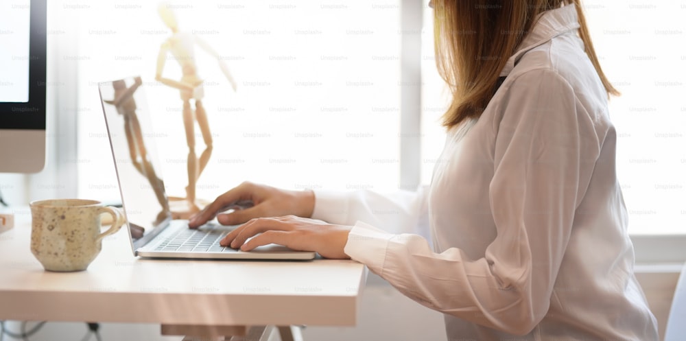Freelancer feminino jovem que trabalha no espaço de trabalho confortável enquanto digita no laptop do teclado
