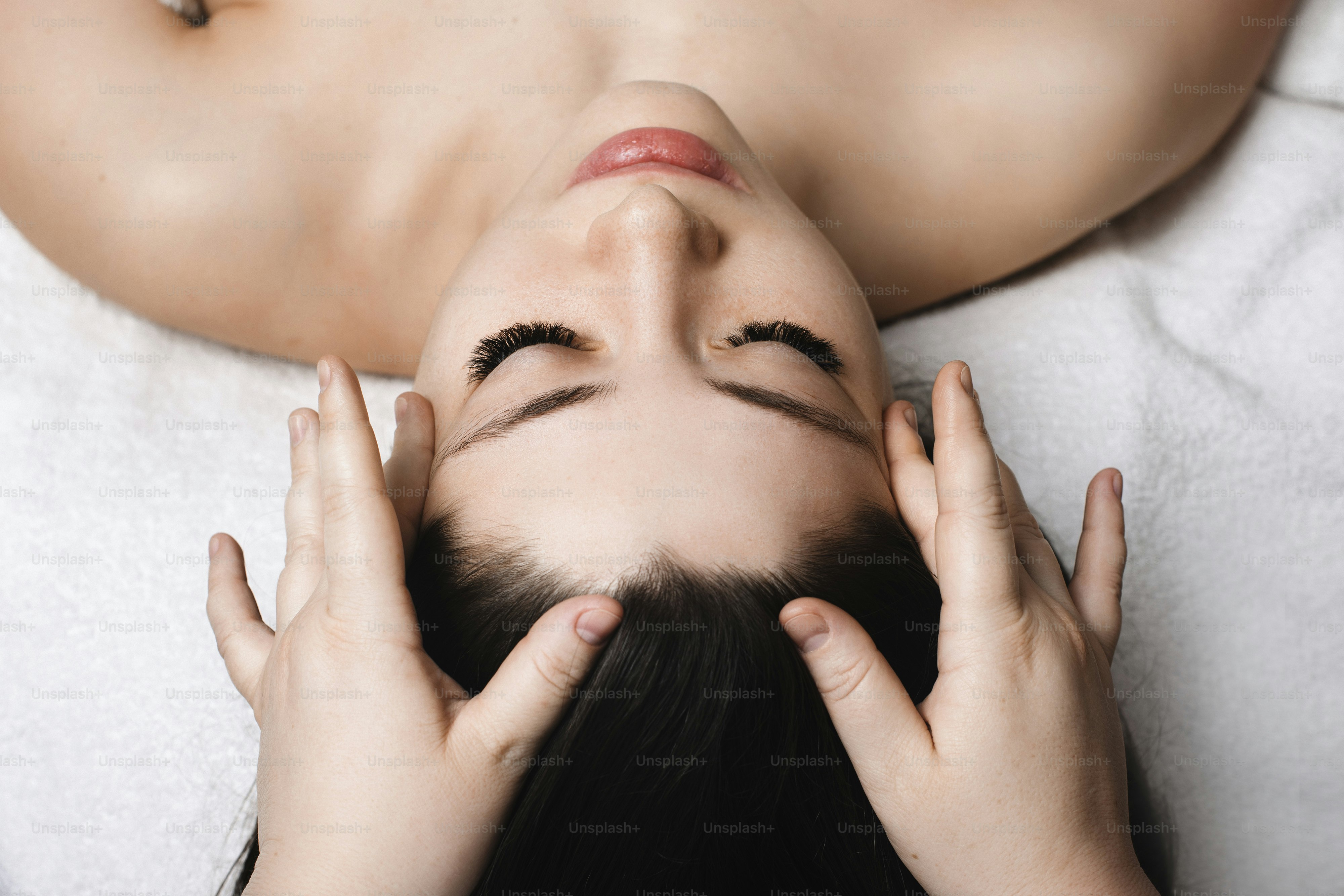 Close up portrait of a young attractive female having skin care facial massage by a cosmetologist in a wellness spa center.