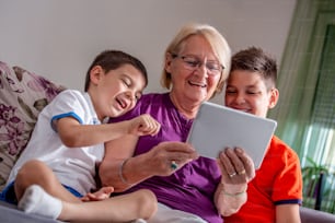 La grand-mère et les petits-fils passent un appel via Internet avec une tablette pour parler en ligne à leur grand-père.