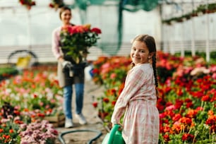 Cute little girl with watering can helping her mother at plant nursery.