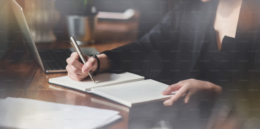 Business woman writing on notebook on table with laptop