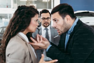 Middle age couple arguing while buying car at car showroom. Car salesman helps them to make right decision.