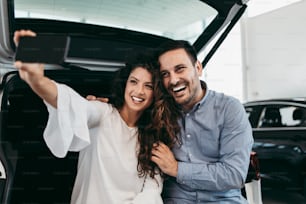 ショールームで新車を選んで購入しながら楽しんでいる幸せな中年夫婦。彼らは自撮り写真を撮ります。