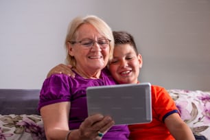 Grandmother with her grandsons on sofa at home. Grandma and children are taking selfie.