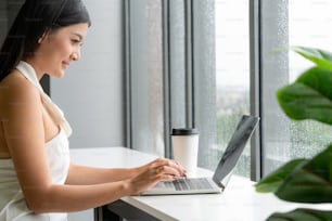 Giovane donna d'affari che utilizza il computer portatile mentre è seduta al tavolo del caffè accanto alle finestre dell'ufficio.