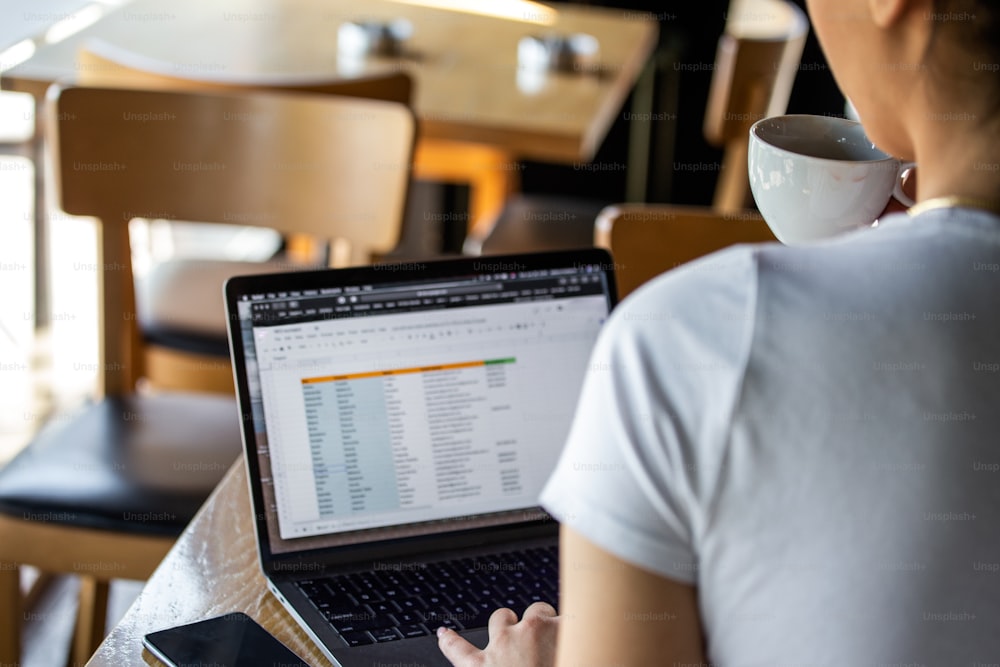 Vista parcial de la escritura de un autónomo en el planificador con el teléfono inteligente y el ordenador portátil en la cafetería