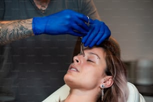 Young Woman getting pierced between her eyes. Man showing a process of piercing with steril medical equipment and latex gloves. Body Piercing Procedure