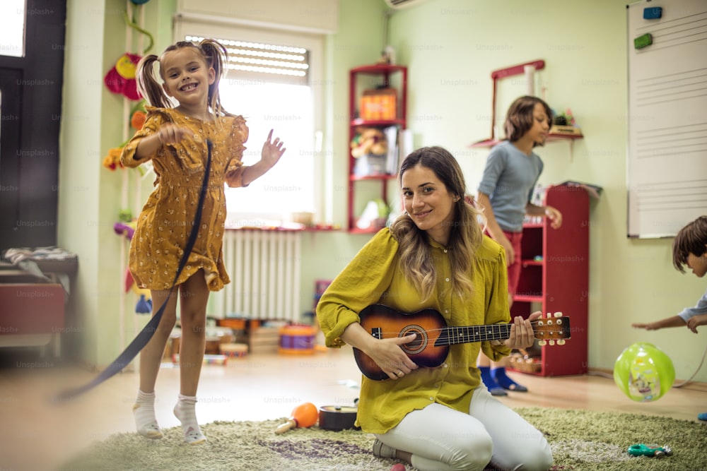 La guitarra libera sonidos maravillosos para el baile. Niños con maestra en preescolar.