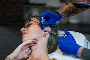 Portrait of a woman getting her nose pierced. Man showing a process of piercing nose with steril neadle and latex gloves. Nostril Piercing Procedure