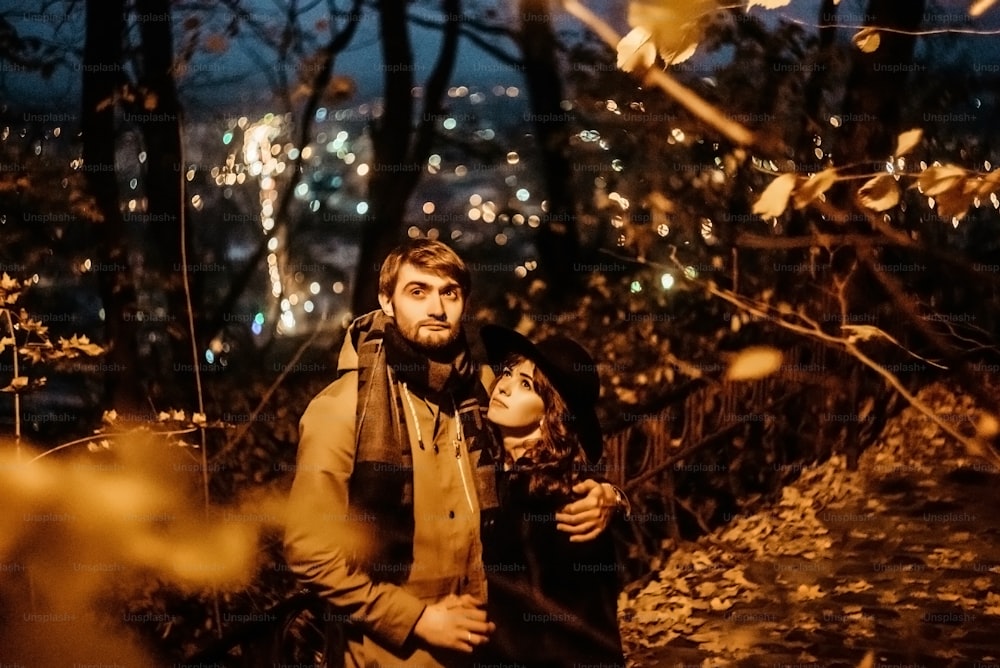 happy stylish couple hugging and holding hands with tender under yellow lantern  in night lights of the city