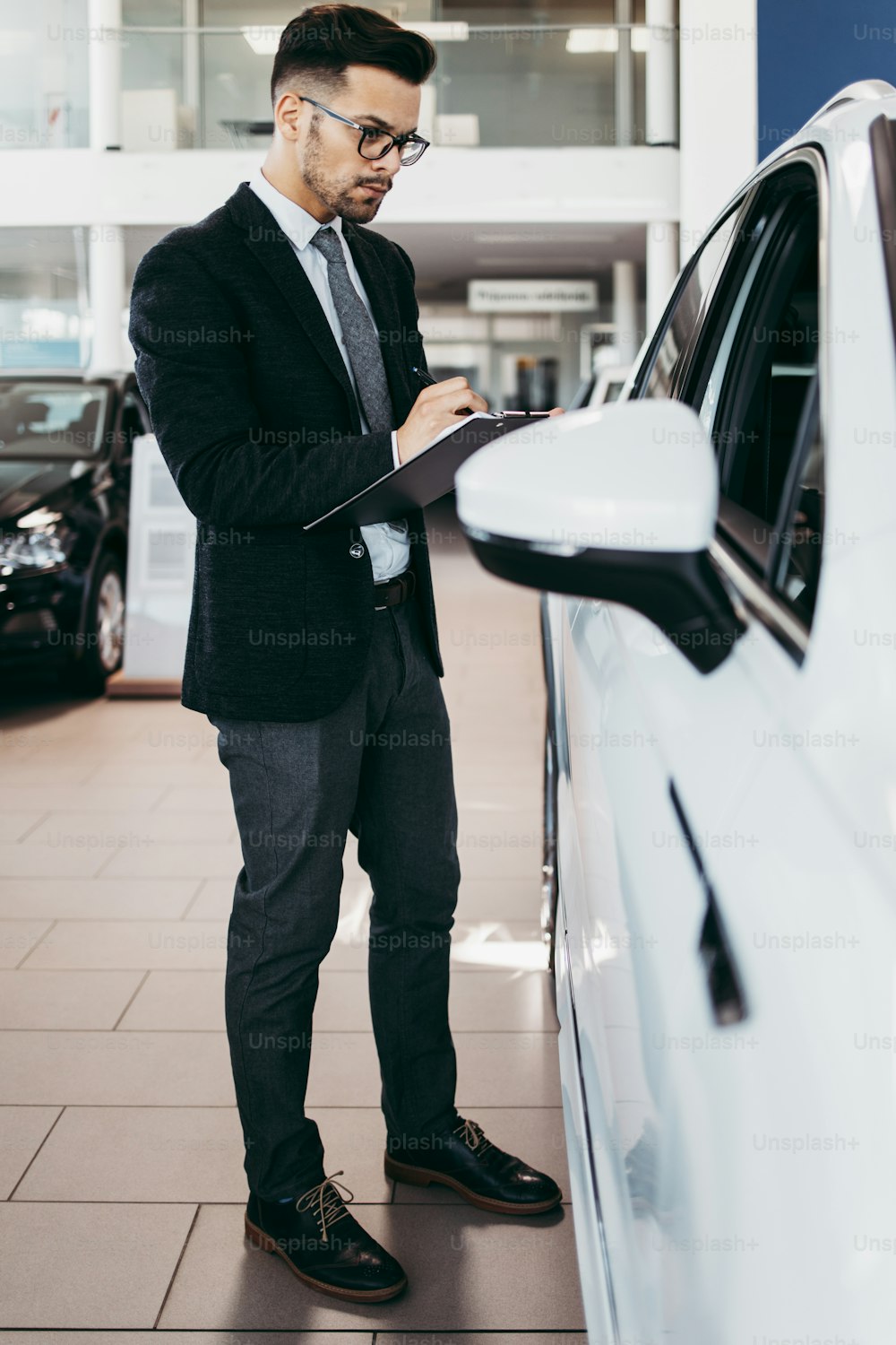 Venditore di auto che lavora in showroom e controllo di qualità dei dettagli dell'auto per l'ultima volta prima che arrivi l'acquirente.