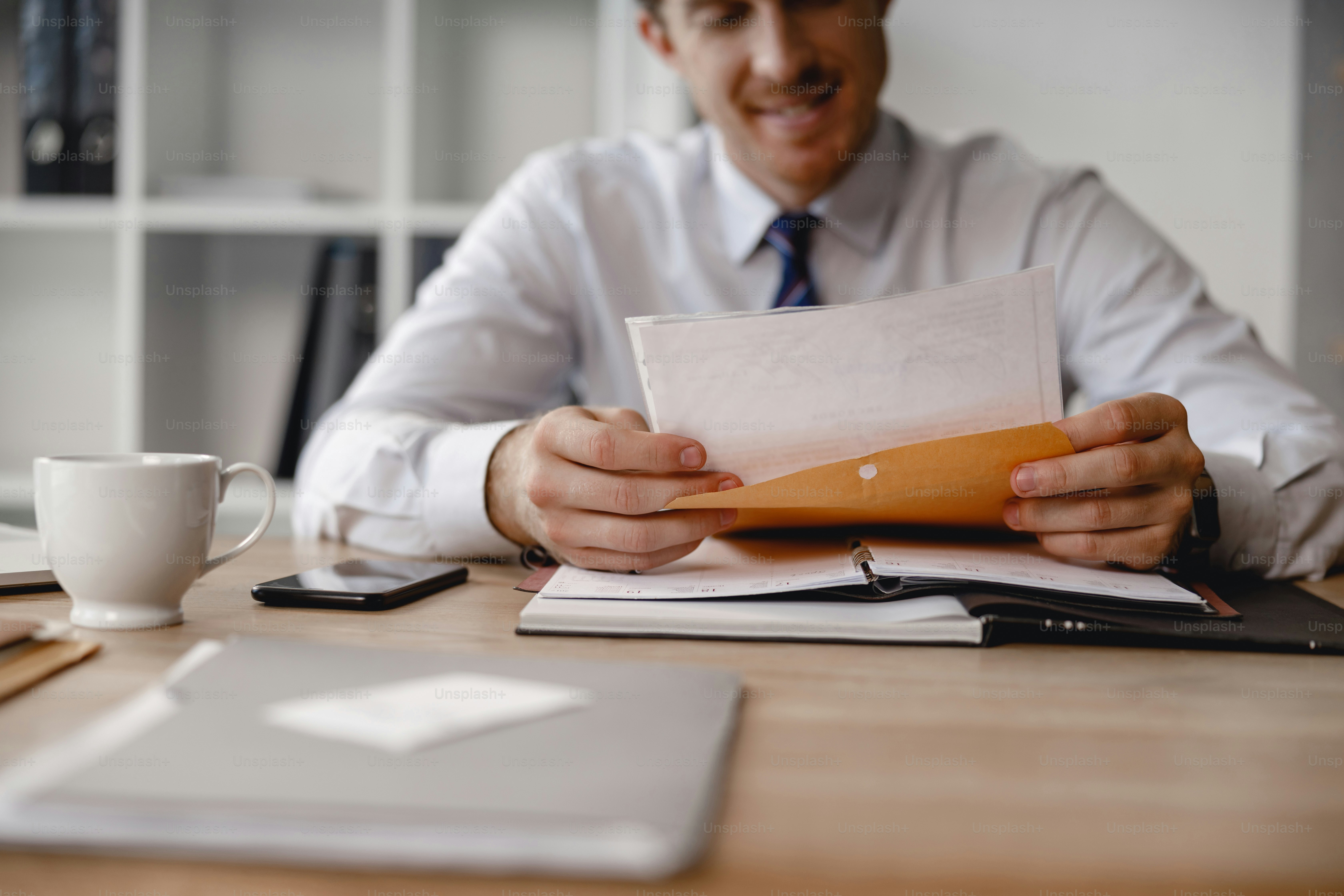 New documents. Cheerful young man sitting at the office table with an envelope in his hands and smiling