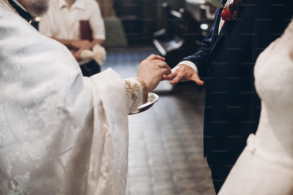 Priester zieht goldene Eheringe an der Hand des Bräutigams in der Kirche während der Hochzeitszeremonie, religiöse Traditionen
