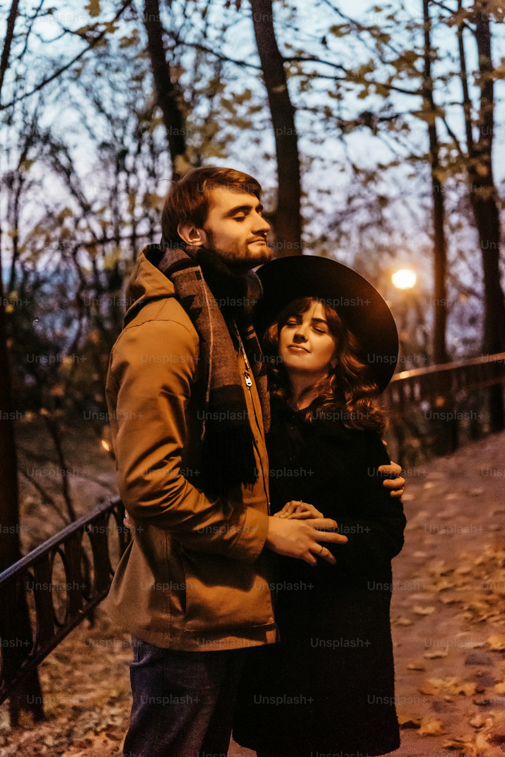 Glückliches, stilvolles Paar, das sich umarmt und Händchen hält, zärtlich unter gelber Laterne in den Nachtlichtern der Stadt