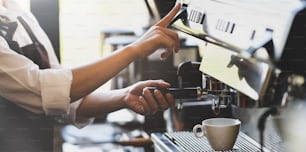 Young female barista working with coffee maker machine in coffee shop