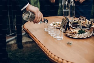 people pouring vodka in glasses on table with food, toasting at wedding reception, celebration outdoors, catering in restaurant. christmas and new year