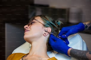 Young Woman getting her ear pierced. Man showing a process of piercing with steril medical equipment and latex gloves. Body Piercing Procedure