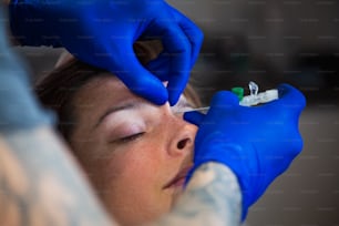 Young Woman getting pierced between her eyes. Man showing a process of piercing with steril neadle and latex gloves. Body Piercing Procedure