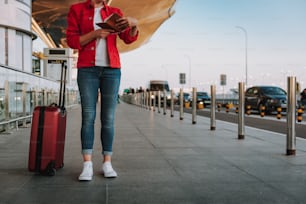 Beschnittenes Porträt einer Dame in roter Jacke, die ein Flugticket hält, während sie auf der Straße steht