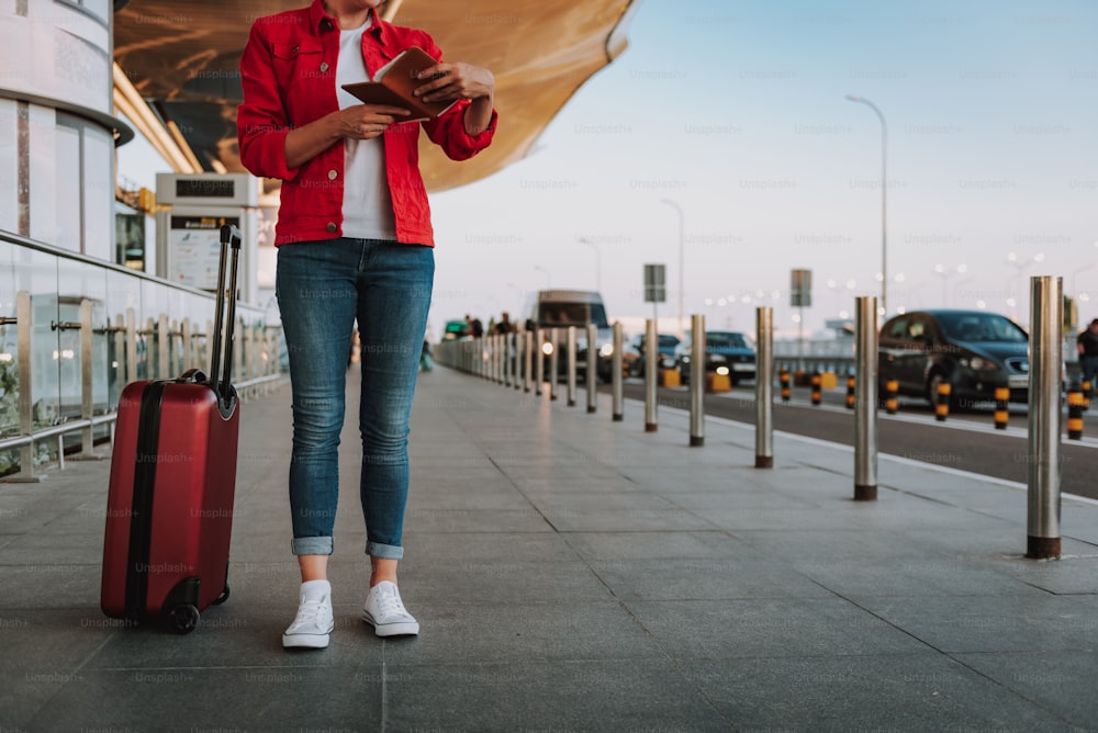 거리에 서 있는 동안 항공권을 들고 있는 빨간 재킷을 입은 여성의 자른 초상화