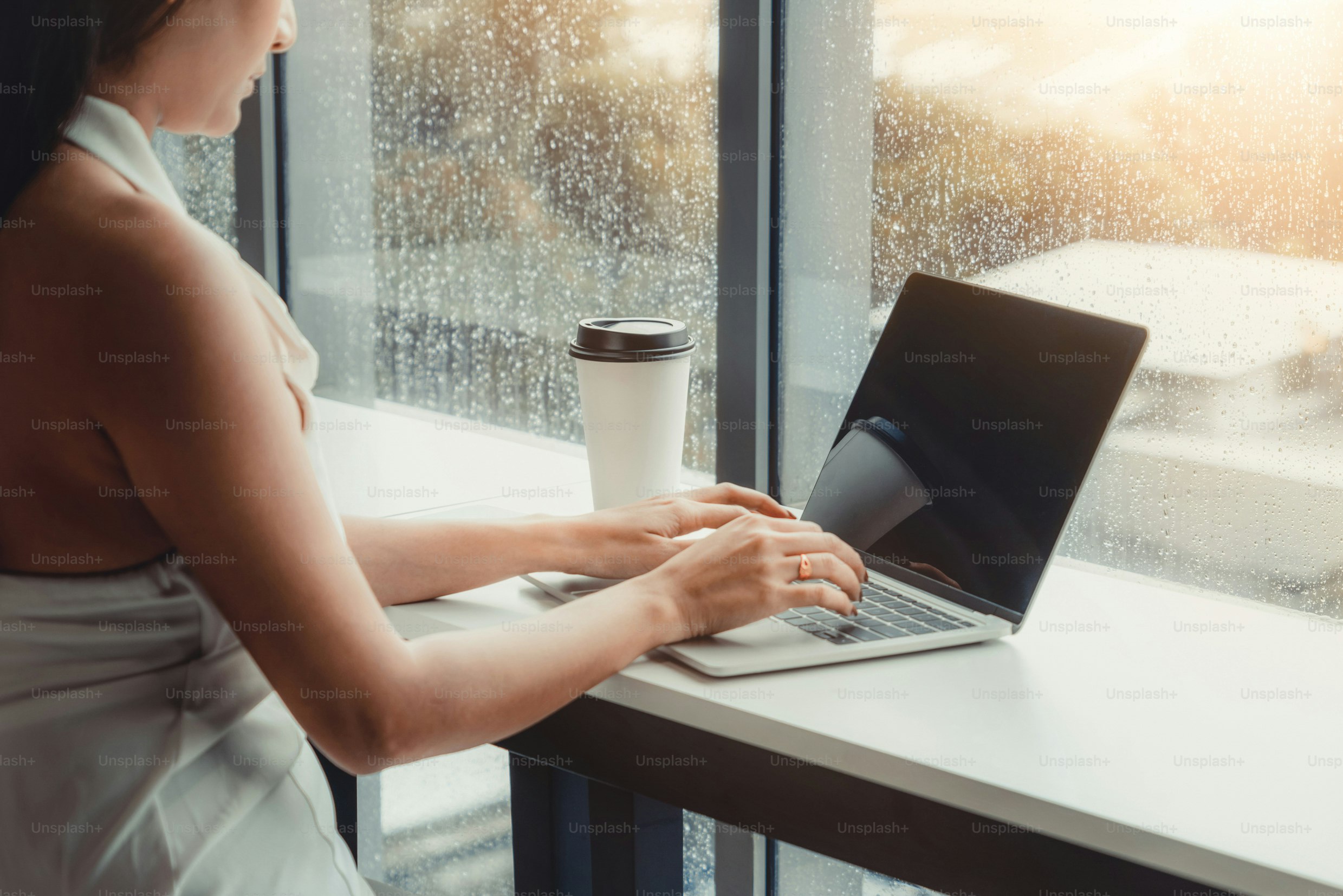 Junge Geschäftsfrau, die einen Laptop benutzt, während sie am Cafétisch neben den Bürofenstern sitzt.