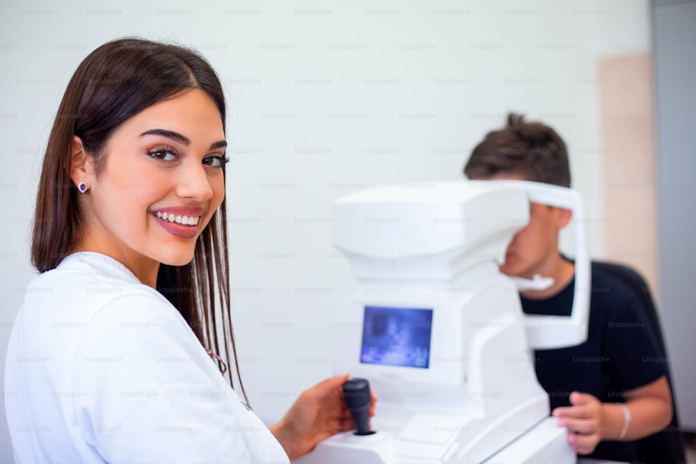 Weibliche Augenärztin, die eine Maschine zur Überprüfung des Sehvermögens in der Klinik verwendet. Kleiner Junge, der sich Geräte anschaut und Augenpupille im Optikergeschäft testet. Konzept der Augenpflege und Gesundheit