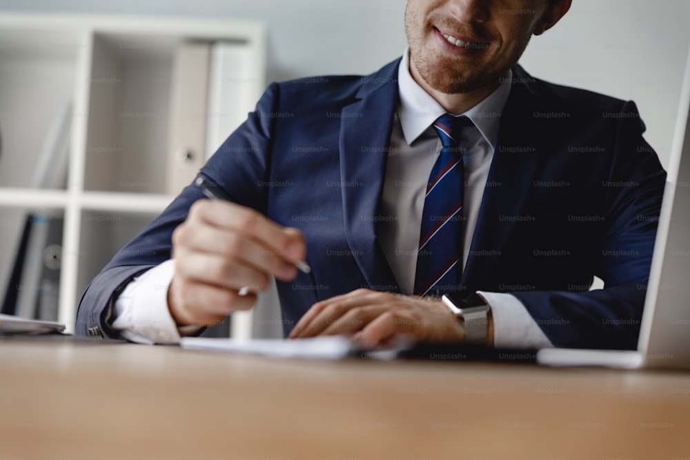Close up of glad man in suit and tie smiling while being at work and making notes