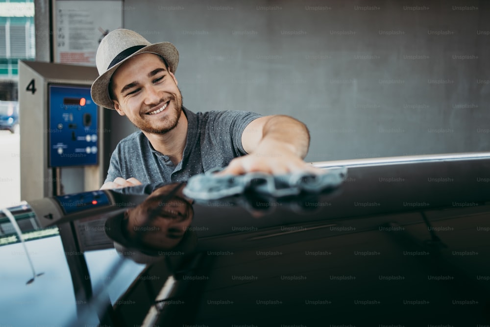 Young handsome man with hat cleaning car with rag, car detailing (or valeting) concept.