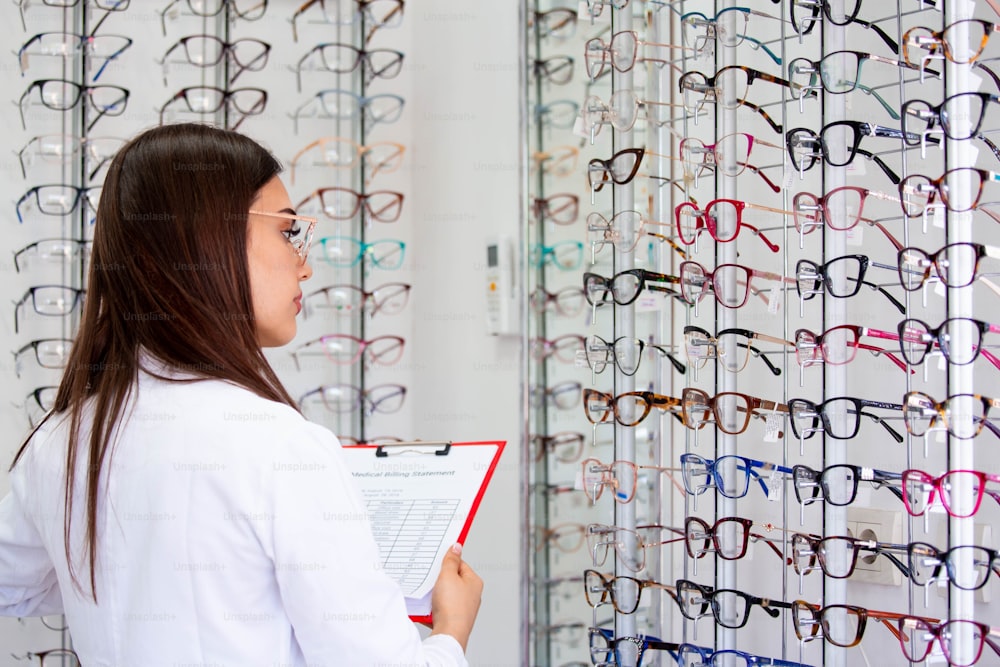 Attractive female ophthalmologist writing data to a clipboard, working in an optical store. Healthcare and medicine concept