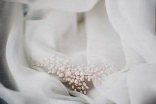 Stylish tender pearl hairpin on soft white tulle in morning light in hotel room. Bridal accessories for the wedding day. Modern jewelry. Morning preparations