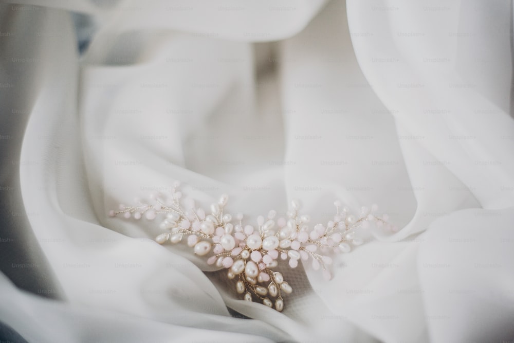 Stilvolle zarte Perlenhaarnadel auf weichem weißem Tüll im Morgenlicht im Hotelzimmer. Brautaccessoires für den Hochzeitstag. Moderner Schmuck. Vormittagsvorbereitungen