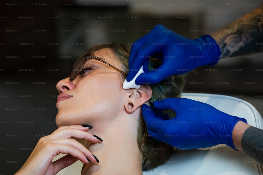 Portrait of a woman getting her ear pierced. Man showing a process of piercing ear with steril neadle and latex gloves. Nostril Piercing Procedure