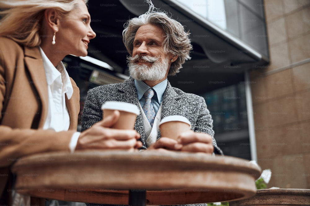 Happy bearded man with coffee to go kindly smiling to a woman next to him