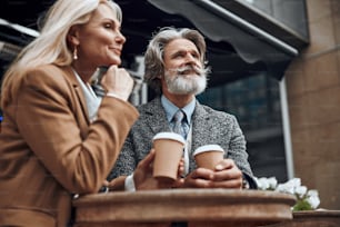 Cheerful bearded man looking away while standing with coffee near his wife
