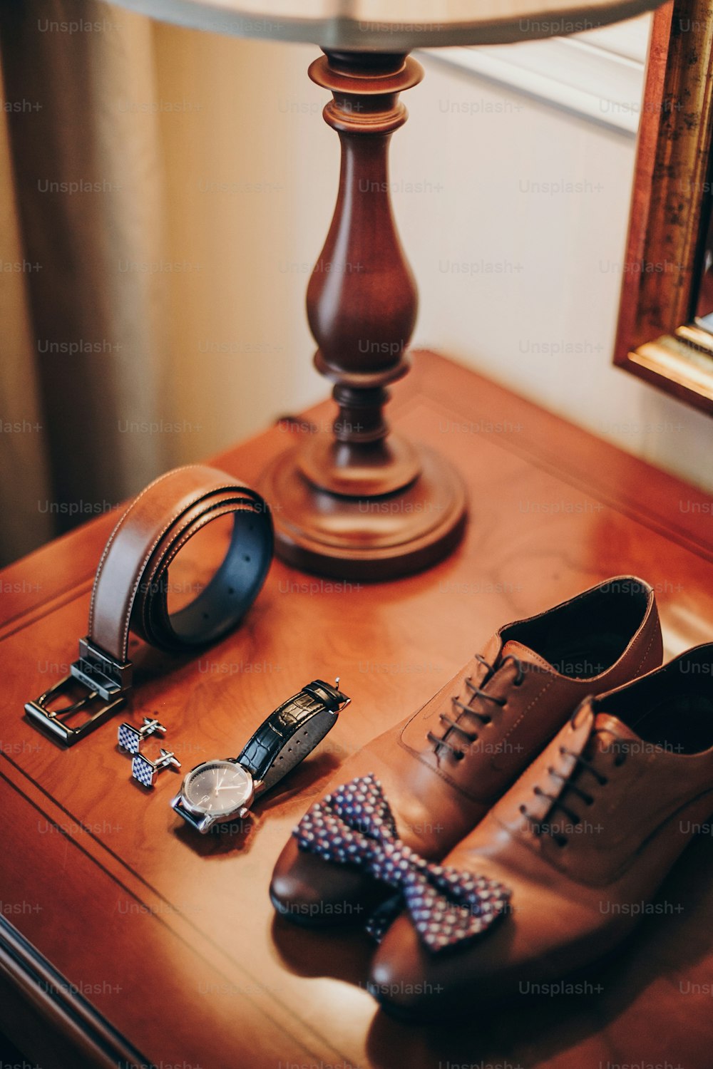 Stylish watch, expensive, shoes, bow tie, cufflinks and belt for groom on wooden table in hotel room. Morning preparation before wedding ceremony. Men accessory for luxury event