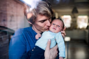 A young father holding a newborn baby at home, kissing. Shot through glass.