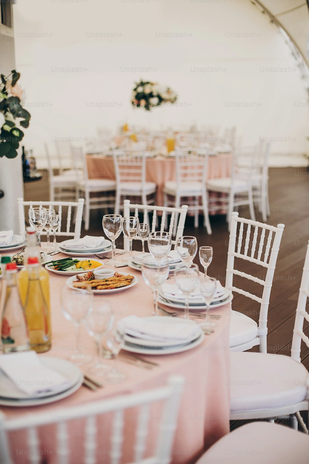 Stylish pink centerpiece with silver cutlery, wine glasses,empty plates, delicious served food on pink cloth at wedding reception in restaurant. Luxury catering