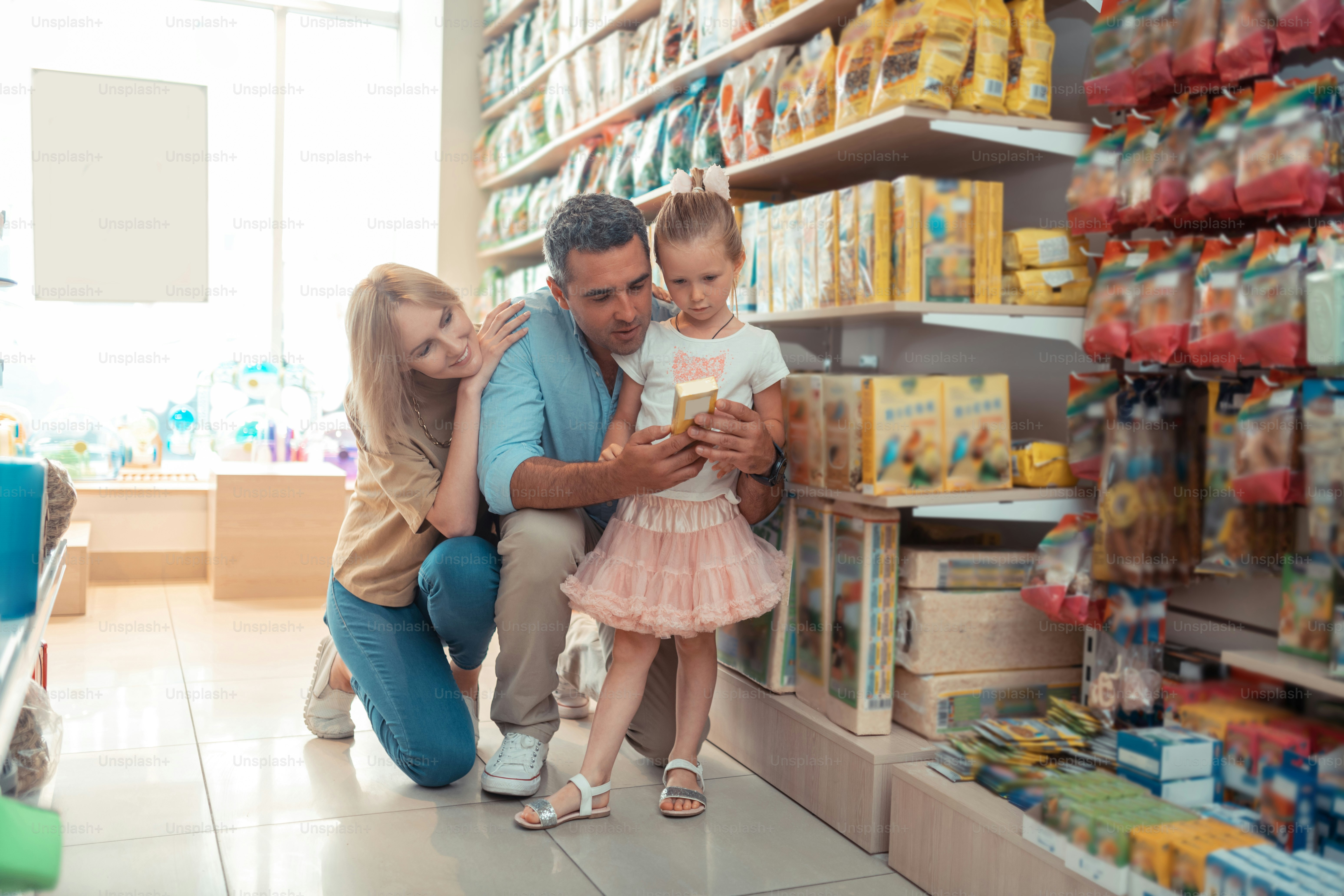 Daughter feeling curious. Daughter wearing pink skirt feeling curious while choosing food for parrot with parents