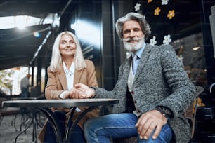 Smiling woman sitting with man in cafe and holding his hand