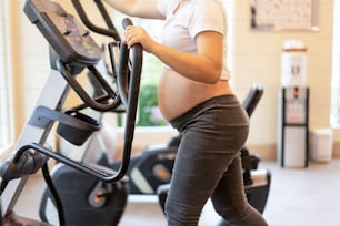 Ejercicio activo de la mujer embarazada en el gimnasio en la sala de yoga. La joven madre embarazada sosteniendo al bebé en el vientre de embarazada. Cuidado prenatal de maternidad y concepto de embarazo femenino.